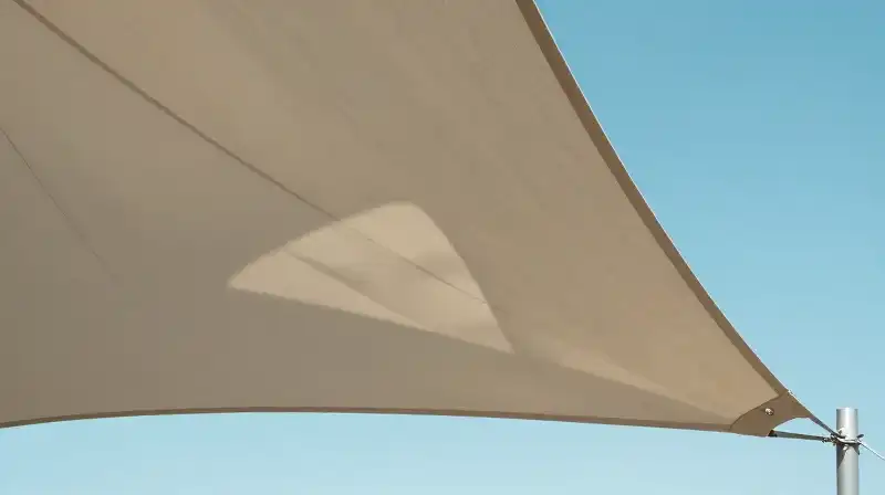 A taut, modern sail casts sharp geometric shadows against a bright blue sky