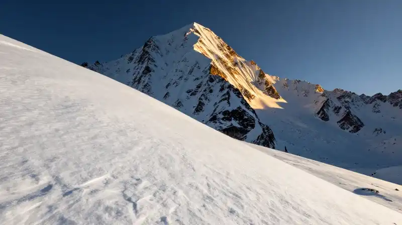 Jagged mountain peak bathed in dramatic golden light amidst untouched snow